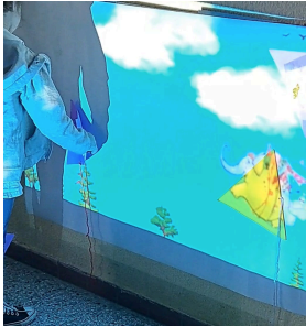 Fotografía de la experiencia inmersiava. Se ve una proyección en la pared de una ilustración del libro y un nene tocandola. 