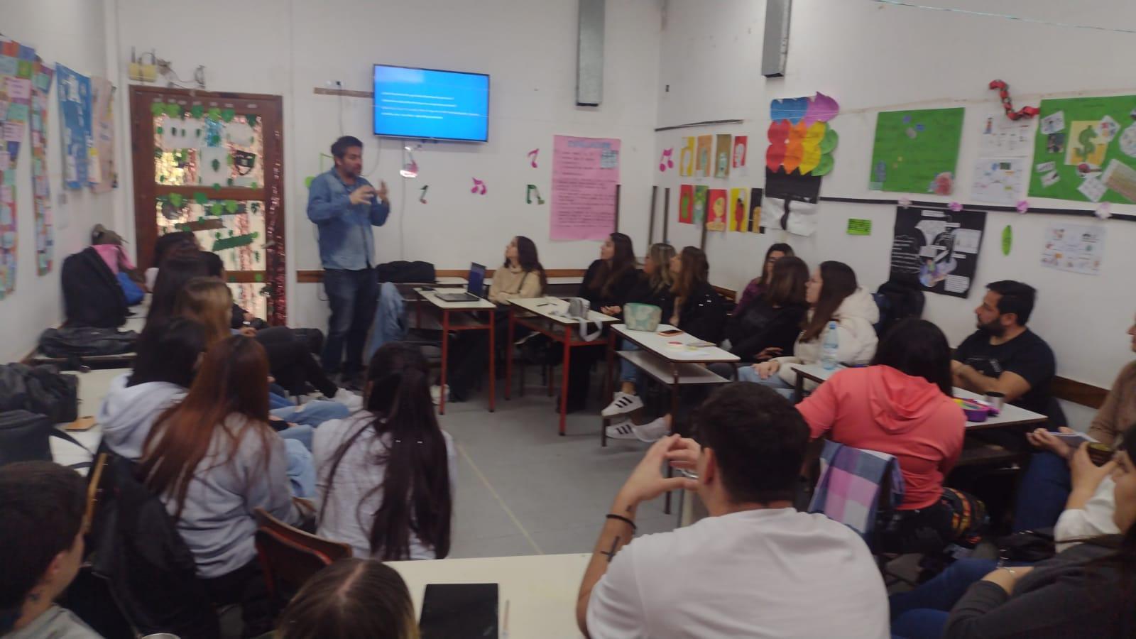 Fotografía de un aula con un docente y estudiantes prestandole atención