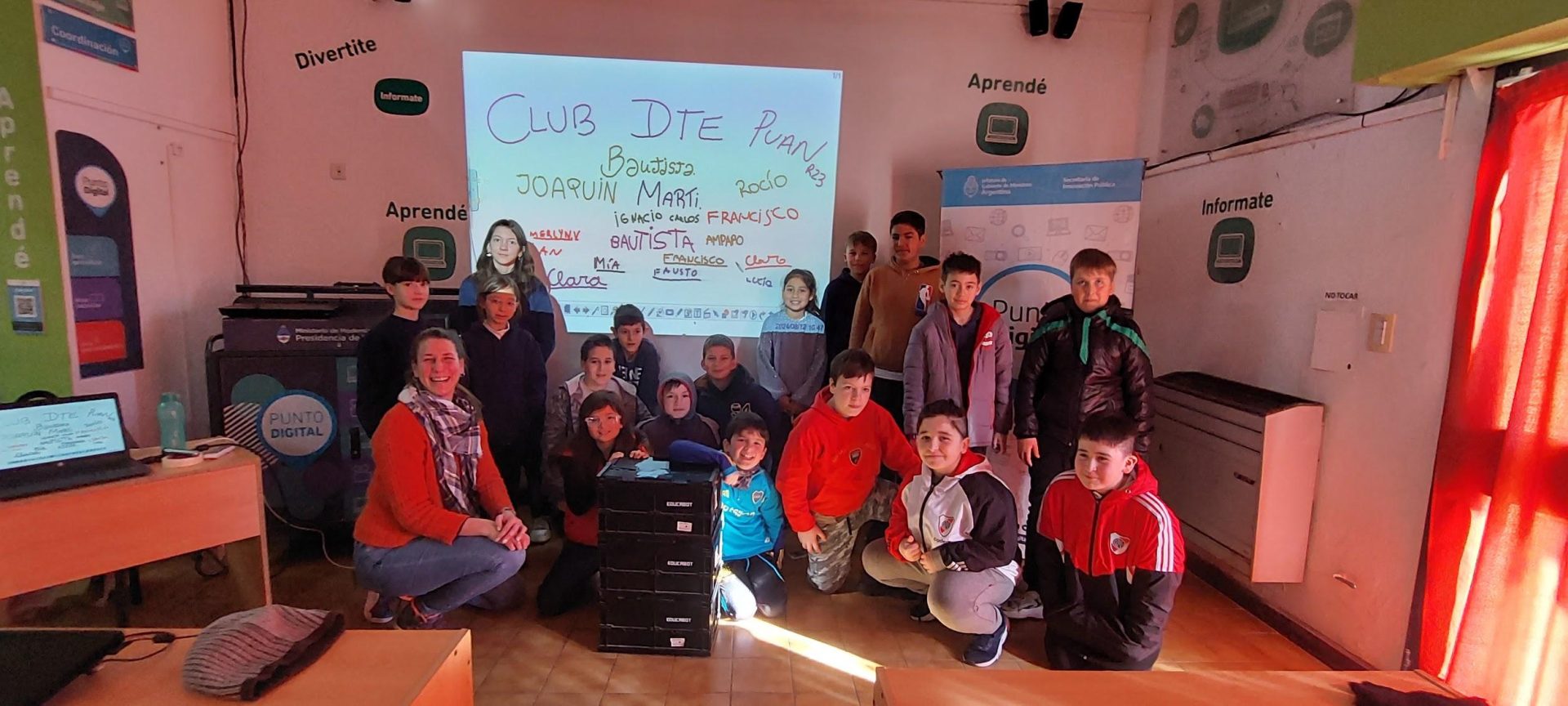 Fotografía de estudiantes con la proyección en una pared de palabras como "Club DTE Puan" y los nombres de los estudiantes.