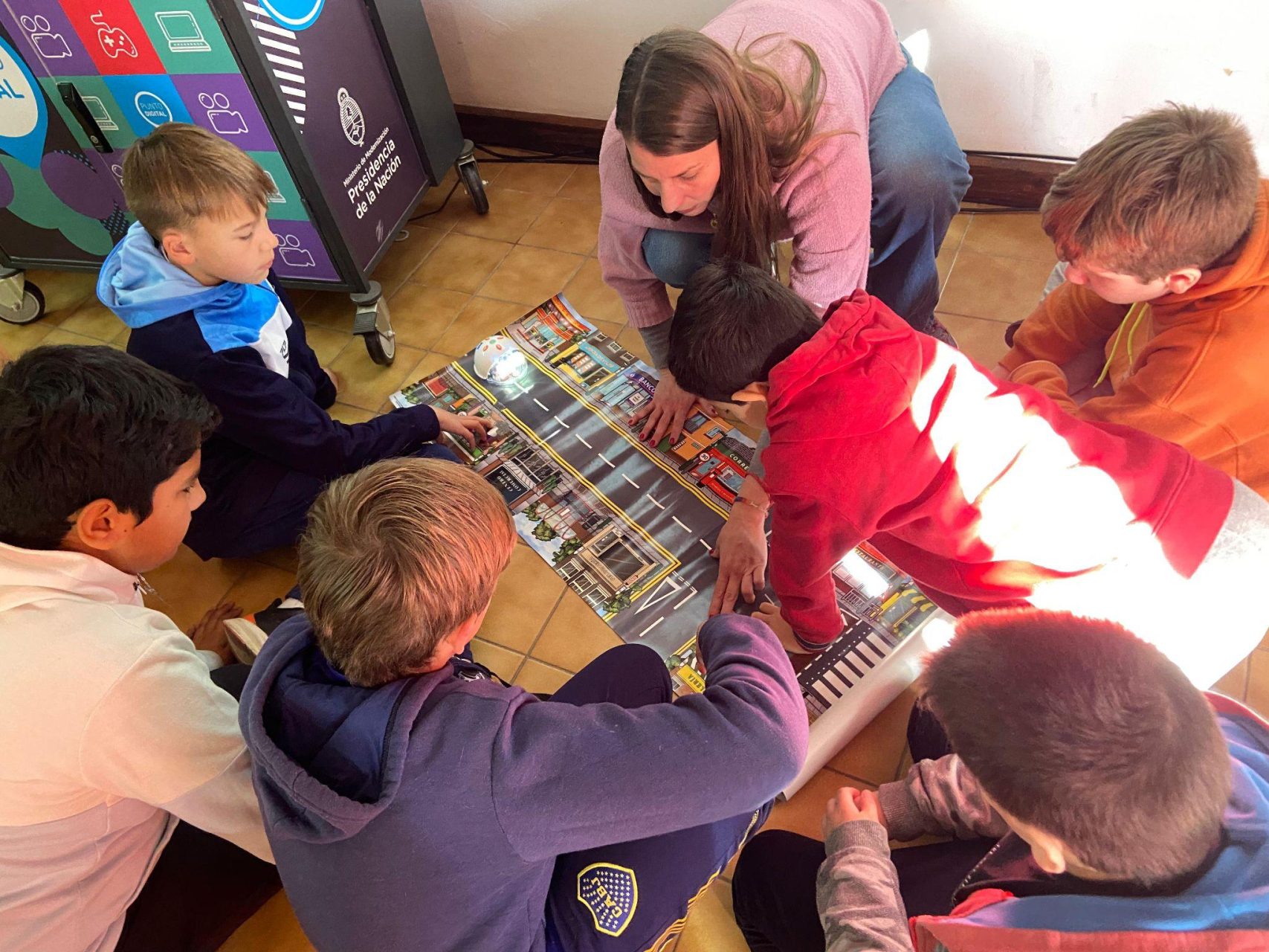 Estudiantes y una docente trabajando en el piso con un robot