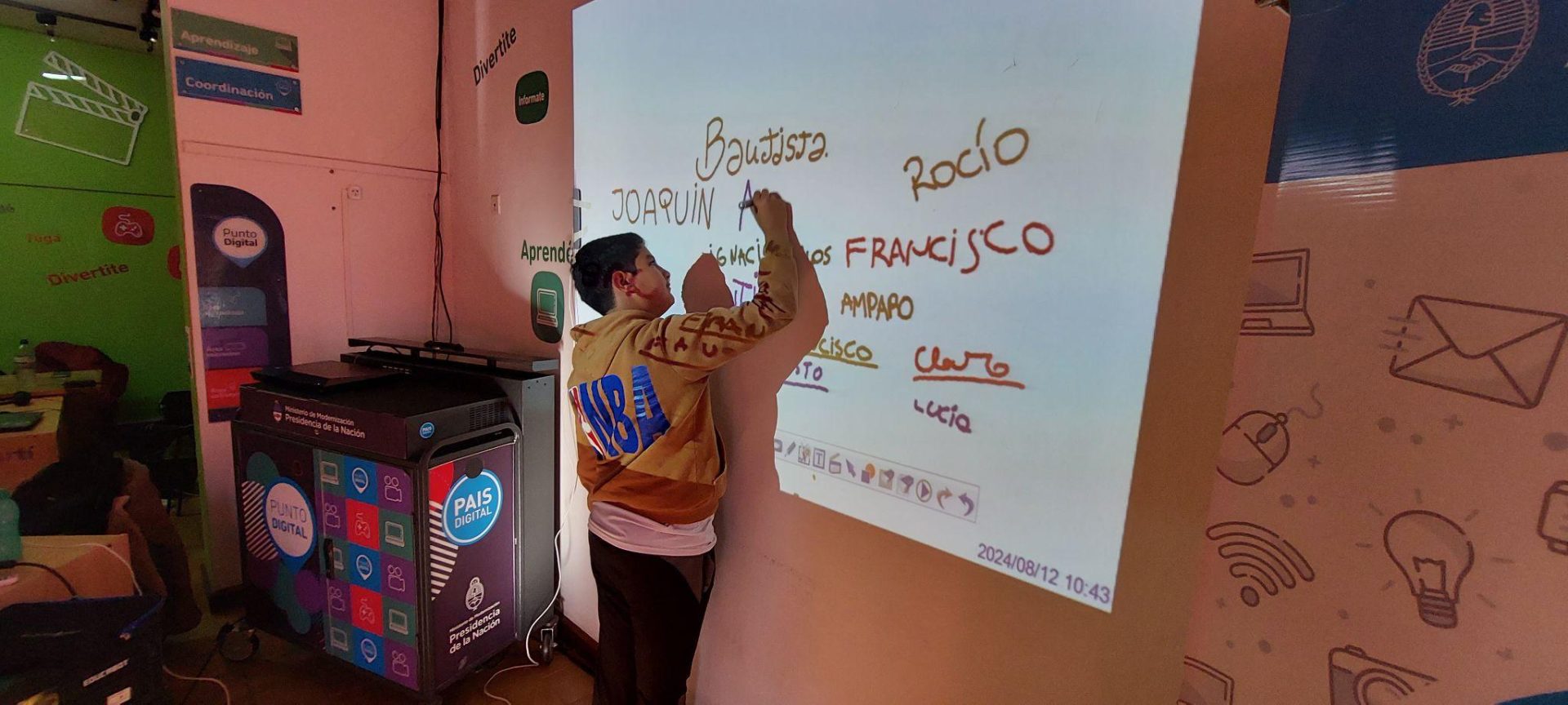 Un chico escribiendo en una proyección en una pared, su nombre.