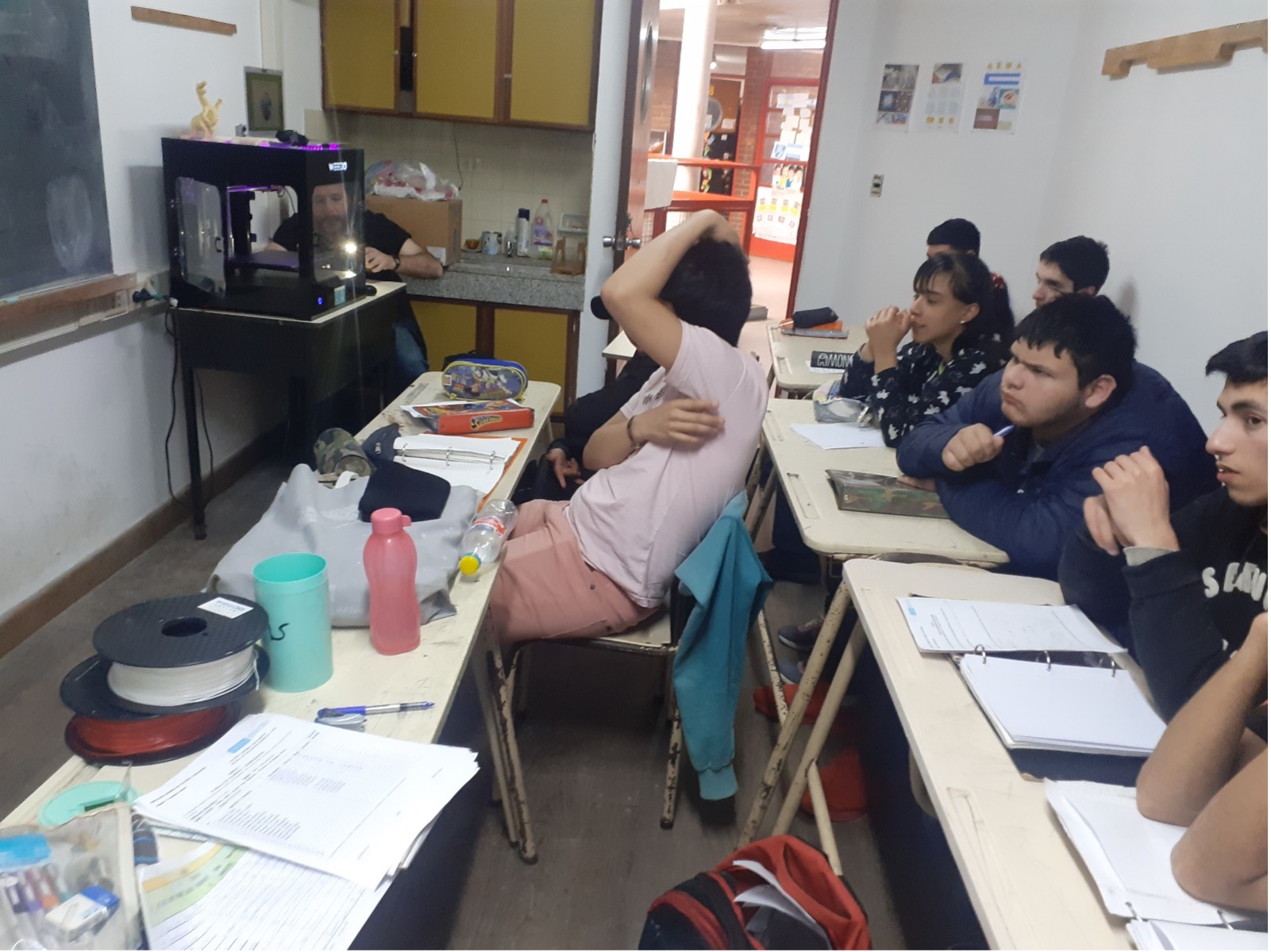 Fotografía de estudiantes en un aula y un docente con una impresora 3D