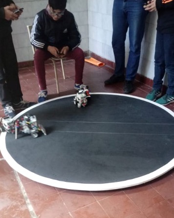 Estudiantes manejando a control dos robots que circulan por una superficie circular