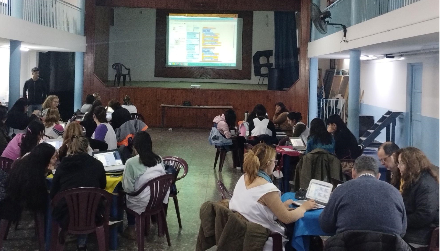 Fotografía de docentes en distintas mesas, trabajando con computadoras