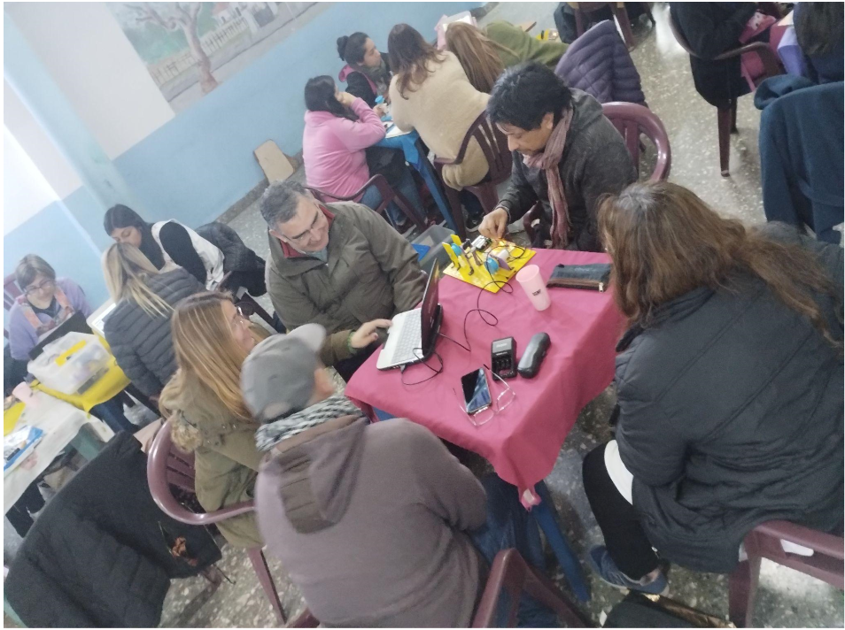 Fotografía de docentes en distintas mesas, trabajando con computadoras y elementos de robótica