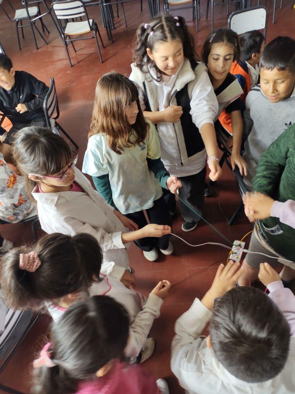 Fotografía de estudiantes agarrando un cable diferente cada uno, los cuales se conectan a una misma placa